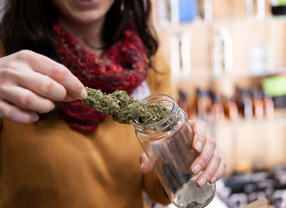 Cannabis Insurance - Customer Opening a Glass Jar and Examining Cannabis Sativa at a Local Cannabis Shop
